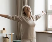 Mujer mayor feliz con los brazos en cruz, disfrutando del envejecimiento activo en su casa