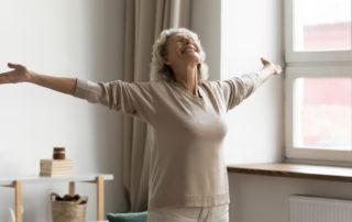 Mujer mayor feliz con los brazos en cruz, disfrutando del envejecimiento activo en su casa
