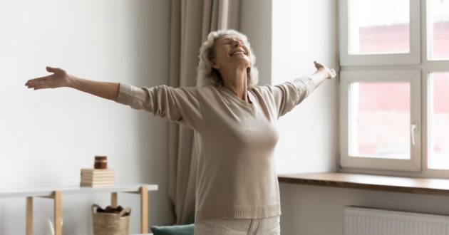 Mujer mayor feliz con los brazos en cruz, disfrutando del envejecimiento activo en su casa
