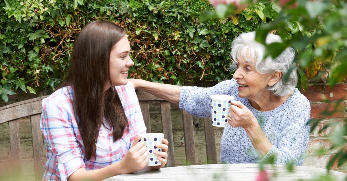 Mujer que realiaz terapias de realidad virtual en personas mayores tomando un café con su nieta en el jardín